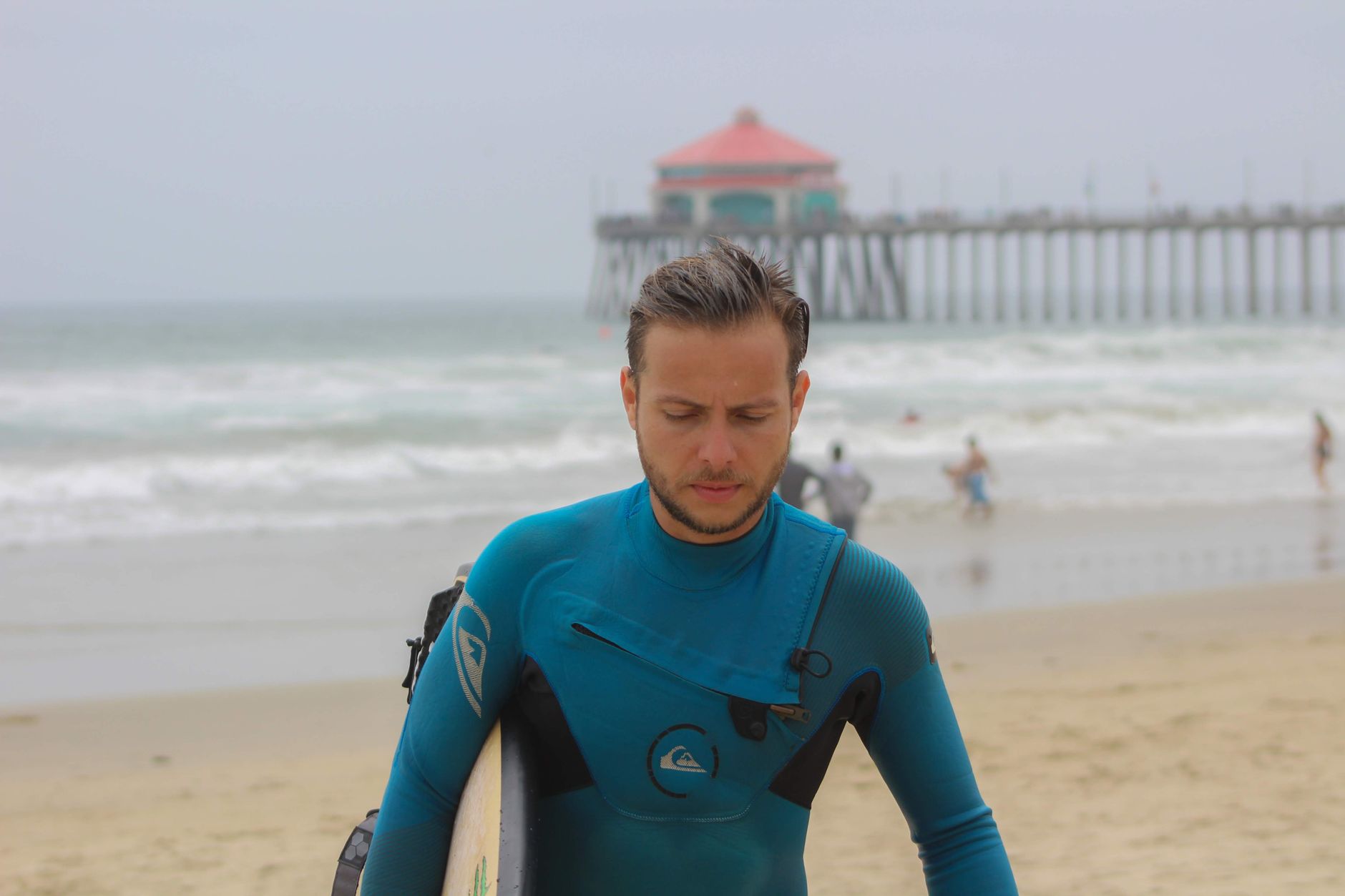Local SEO in Huntington Beach, CA near Huntington Pier | OCWebPros. A surfer walks on Huntington Beach with the iconic pier i
